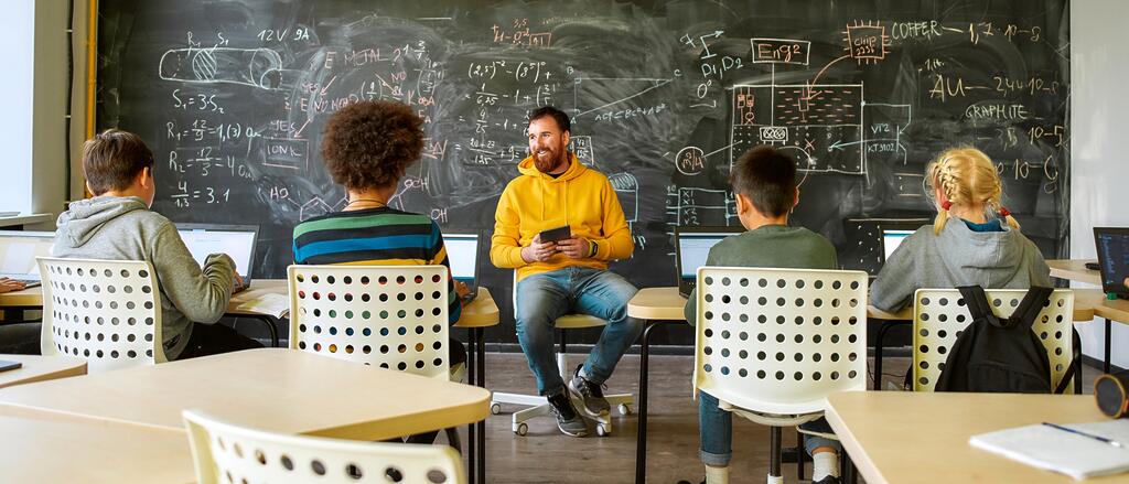 Private Endgeräte im Dienstgebrauch Lehrer sitzt mit einem Tablet vor vier Schülern im Klassenzimmer